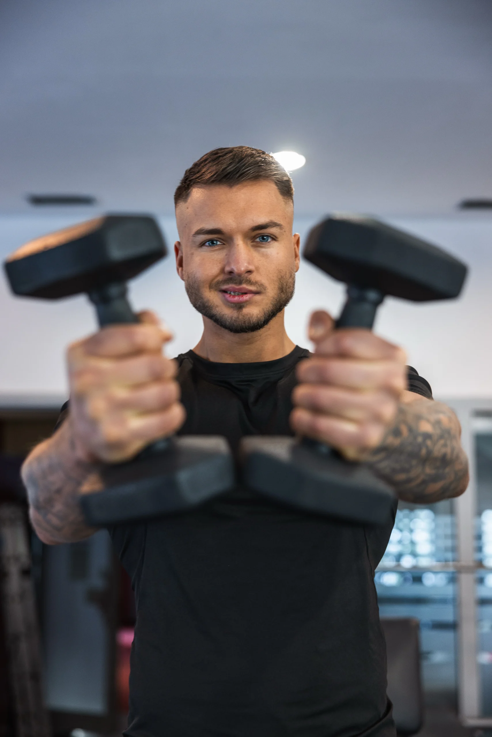 Trener Michał trzymający przed sobą dwa hantle na tle siłowni.